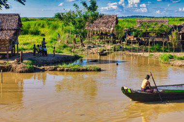 Bago, Myanmar - 03 Aralık 2012: Güneşli bir günde Myanmar 'daki kırsal evlerin yakınlarındaki sakin suda kürek çeken bir kayıkçı varken çocuklar nehir kıyısında oynuyorlar.
