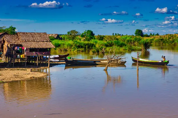 Bago, Myanmar - Aralık 03 2012: Balıkçılar, Myanmar 'ın sakin suları boyunca, parlak mavi gökyüzünün altında, ahşap bir ev yakınlarında teknelerini yüzdürürler..