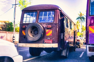 Yangon, Myanmar - 02 Aralık 2012: Yangon Myanmar 'da her iki tarafında arabalarla dolu işlek bir caddede parlak bir gökyüzü altında eski model bir otobüs geziniyor.