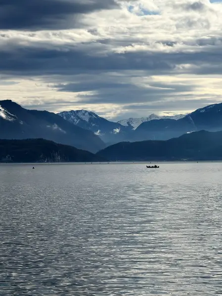 Ek bina, Fransa - 5 Ocak 2025: Bulutlu gökyüzü sakin suyun üzerinde beliriyor ve uzak dağları yansıtıyor..