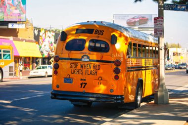 Los Angeles, ABD - 24 Ekim 2009: Los Angeles 'ta yol kenarında renkli duvar resimleri ve şehir yaşamını gösteren tabelalarla canlı sarı bir otobüs duruyor.