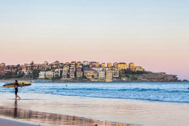 Bondi Plajı, Avustralya - 20 Ekim 2009: Bir sörfçü, Sidney Avustralya 'da gün batımında kumsala vuran dalgalarla Bondi Sahili' nin sakin kıyı şeridi boyunca yürüyor.