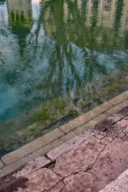 Ek bina, Fransa - 10 Ocak 2020: Sakin sular Annecy Haute Savoie 'deki ağaç ve binaları yansıtıyor ve bölgede sakin bir atmosfer yaratıyor.