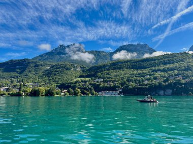 Talloires, Fransa - Eylül 06 2024: Sakin bir öğleden sonra, Berrak turkuaz suları Annecy 'nin bereketli dağlarını yansıtırken, bir tekne göl yüzeyinde huzur içinde süzülüyor,