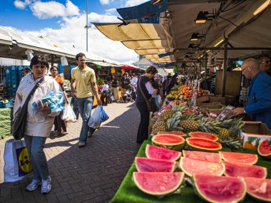 Den Haag, Hollanda - Haziran 02 2009: İnsanlar güneşli bir günde açık hava pazarından alışveriş yapıyorlar. Karpuzlar ve ananaslar satıcıların masasında belirgin bir şekilde sergilenir..