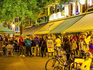 Den Haag, Hollanda - Haziran 2009: Akşam sosyalleşmesinin keyfini çıkaran bir grup insan. Masalardaki restoranlar. Hollanda 'da cadde boyunca park etmiş bisikletler..