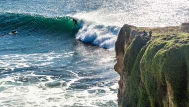 Santa Cruz, ABD - 27 Ocak 2013: Sörfçü dev bir dalgada sörf yaparken, diğer bir kişi Kaliforniya 'da okyanusa bakan kayalıklardan hayranlık duyuyor.