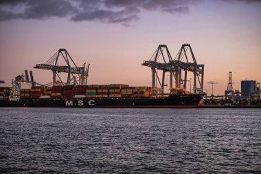 Rotterdam, Hollanda - 22 Kasım 2021: Gün batımında Rotterdam 'da bir konteynır gemisinden konteynır indirmek için büyük vinçler çalışıyor.