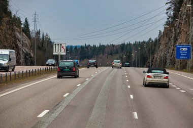 Oslo, Norveç - 25 Nisan 2012: Arabalar bulutlu bir günde Oslo Norveç 'te ağaçlar ve kayalık arazilerle çevrili geniş bir otoyol boyunca seyahat ederler.