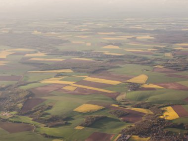 An aerial view captures vibrant fields in various shades of green and yellow showcasing agricultural patterns and rural landscape.