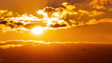 Time lapse bright orange sunset sun sets behind the clouds. The end of the day, the sun goes below the horizon. Big red hot sun in warm air distortion above the horizon.
