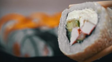 Sushi dürümleri yakın plan suşi için yemek çubuklarıyla alınır. Bir restoranda Japon mutfağı suşisi. Somon ve sebzeli suşi. Japon restoran menüsü. Yan görünüm.