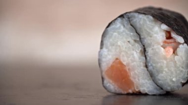 Bir suşi rulosu siyah bir kabın içinde dönüyor. Bir restoranda Japon mutfağı suşisi. Somon ve sebzeli suşi. Japon restoran menüsü. Yan görünüm.