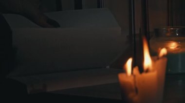 Kadınların elleri mum ışığında eski bir kitabı karıştırır. Sarı mumlarla dolu eski kütüphanenin atmosferi. Düşük ışıkta eski bir kitabın gece okuması. Geceleri kütüphane, eski edebiyat kitapları..