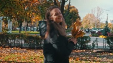 Genç mutlu kadın sonbahar parkında akçaağaç yapraklarıyla kıvrılır. Bir kız güneşli bir parkta bir buket sonbahar yaprağı topluyor. Sonbahar sarı yaprakları koleksiyonu, sonbahar parkında yürüyüş..