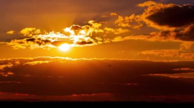 Time lapse bright orange sunset sun sets behind the clouds. The end of the day, the sun goes below the horizon. Big red hot sun in warm air distortion above the horizon.