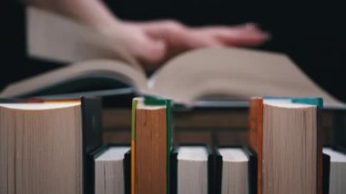 Young girl reads a book on the background of a shelf with books. Library bookshelves background stack of books. The pages of the book are turning. Reading scientific literature surrounded by books.