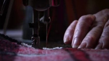 Needle and foot of the sewing machine penetrate the fabric close-up. An aged woman with glasses sews on an old sewing machine. A seamstress makes a machine-made even seam on a red fabric.