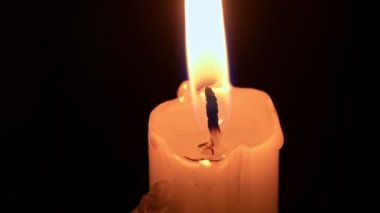 Paraffin candle burns in the dark with a yellow flame. A large fire in a wax candle burns yellow. There is no light in the house, heat from a candle. Poverty, war, a moment of silence.