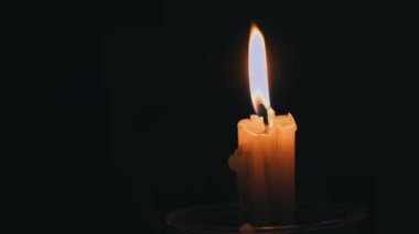 Paraffin candle burns in the dark with a yellow flame. A large fire in a wax candle burns yellow. There is no light in the house, heat from a candle. Poverty, war, a moment of silence.