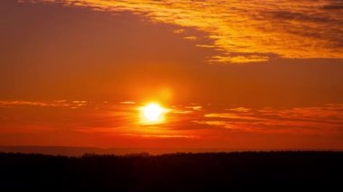 Parlak turuncu gün batımı bulutların arkasında batıyor. Günün sonunda, güneş ufkun altına batar. Ufkun yukarısındaki sıcak hava bükümünde büyük kırmızı güneş..