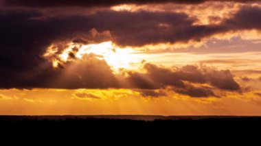 Parlak turuncu gün batımı bulutların arkasında batıyor. Günün sonunda, güneş ufkun altına batar. Ufkun yukarısındaki sıcak hava bükümünde büyük kırmızı güneş..