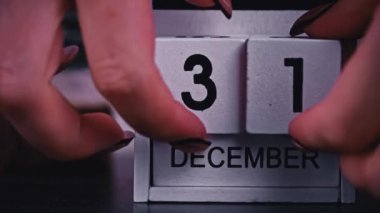 Womans hand changes the date on a white wooden calendar to the new year. New year date 2023 and winter atmosphere. Wooden calendar with an important event from December 31st to January 1st.