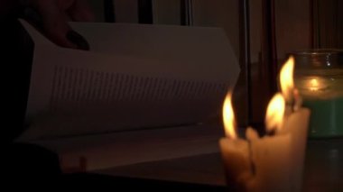 Kadınların elleri mum ışığında eski bir kitabı karıştırır. Sarı mumlarla dolu eski kütüphanenin atmosferi. Düşük ışıkta eski bir kitabın gece okuması. Geceleri kütüphane, eski edebiyat kitapları..