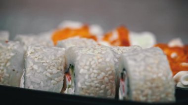 Sushi roll is spinning in a black container close-up. Japanese cuisine sushi in a restaurant. Sushi roll with salmon and vegetables. Japan restaurant menu. Side view.