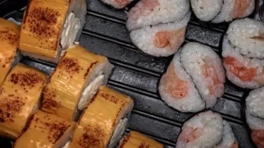 Suşi rulosu siyah bir kapta yakın plan çekimde dönüyor. Bir restoranda Japon mutfağı suşisi. Somon ve sebzeli suşi. Japon restoran menüsü. Yukarıdan görüntüle.
