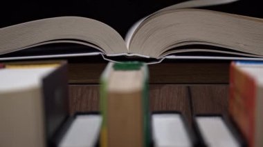 Young girl reads a book on the background of a shelf with books. Library bookshelves background stack of books. The pages of the book are turning. Reading scientific literature surrounded by books.