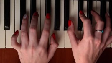 Female hands with fingers play the piano keyboard close-up top view. The piano keys are black and white. Musical instrument, spiritual education, calm music.