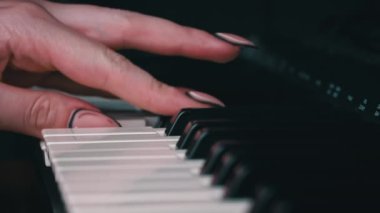Female hands with fingers play the piano keyboard close-up side view. The piano keys are black and white. Musical instrument, spiritual education, calm music.