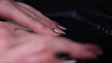 Female hands with fingers play the piano keyboard close-up side view. The piano keys are black and white. Musical instrument, spiritual education, calm music.