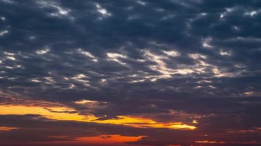 Parlak turuncu gün batımı bulutların arkasında batıyor. Günün sonunda, güneş ufkun altına batar. Ufkun yukarısındaki sıcak hava bükümünde büyük kırmızı güneş..
