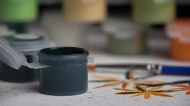 Acrylic paints of different colors stand on the canvas ready to be painted. A hand with a manicure paints empty cells by numbers. Paint brush and draws a picture with acrylic paints.