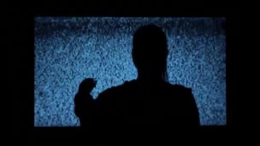 Silhouette of a girl watching TV with noises, shot from the back. Watching TV is a static glitch. Silhouette of a girl watching TV with static noise. Shot behind the shoulders of the model.