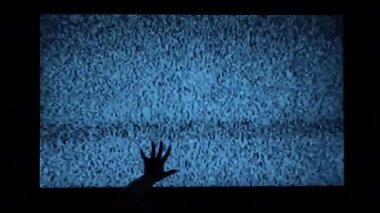 Hands on the background of the noise of the TV scary scene for a horror movie. Scary witchs hands climb the TV screen. Silhouette of hands with claws and interference on the TV screen.