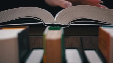 Young girl reads a book on the background of a shelf with books. Library bookshelves background stack of books. The pages of the book are turning. Reading scientific literature surrounded by books.