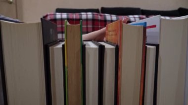 Young girl chooses a book on a shelf with books. Library bookshelves background stack of books. The pages of the book are turning. Reading scientific literature surrounded by books.