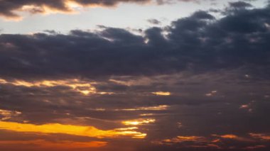 Parlak turuncu gün batımı bulutların arkasında batıyor. Günün sonunda, güneş ufkun altına batar. Ufkun yukarısındaki sıcak hava bükümünde büyük kırmızı güneş..