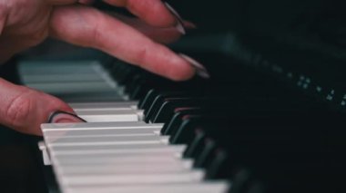 Female hands with fingers play the piano keyboard close-up side view. The piano keys are black and white. Musical instrument, spiritual education, calm music.