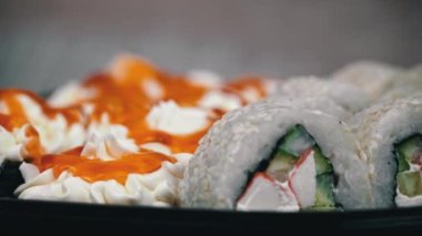 Sushi roll is spinning in a black container close-up. Japanese cuisine sushi in a restaurant. Sushi roll with salmon and vegetables. Japan restaurant menu. Side view.