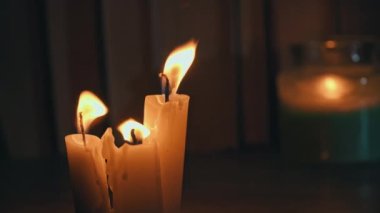 Candles burn in dark against background of a shelf with old books. Atmosphere of old library with yellow candles. Night reading of an old book in low light. Library at night, reading old literature.