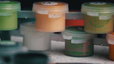Acrylic paints of different colors stand on the canvas ready to be painted. A hand with a manicure paints empty cells by numbers. Paint brush and draws a picture with acrylic paints.