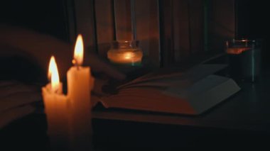 Kadınların elleri mum ışığında eski bir kitabı karıştırır. Sarı mumlarla dolu eski kütüphanenin atmosferi. Düşük ışıkta eski bir kitabın gece okuması. Geceleri kütüphane, eski edebiyat kitapları..
