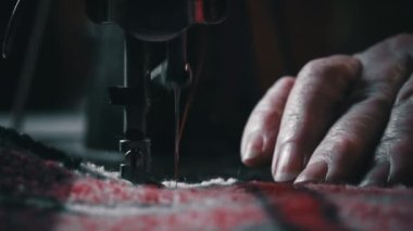 Needle and foot of the sewing machine penetrate the fabric close-up. An aged woman with glasses sews on an old sewing machine. A seamstress makes a machine-made even seam on a red fabric.