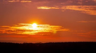 Parlak turuncu gün batımı bulutların arkasında batıyor. Günün sonunda, güneş ufkun altına batar. Ufkun yukarısındaki sıcak hava bükümünde büyük kırmızı güneş..