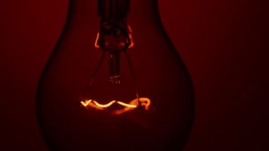Light bulb lights up and goes out on a red background in the dark. Slow turning on and off of a tungsten light bulb. Filament of a blinking vintage light bulb. Energy, electricity, light, life.