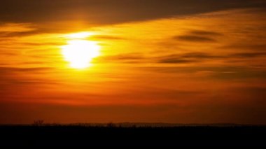 Parlak turuncu gün batımı bulutların arkasında batıyor. Günün sonunda, güneş ufkun altına batar. Ufkun yukarısındaki sıcak hava bükümünde büyük kırmızı güneş..